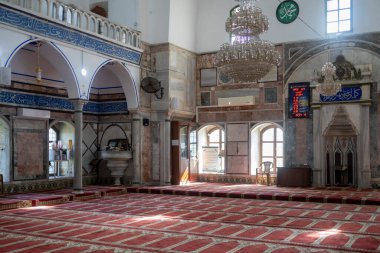 kko, İsrail - 23 Ocak 2025, El Cezire Camii 'nin içinde kırmızı halılar ve namaz saatlerini gösteren bir duvar paneli.