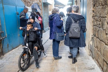 Akko, İsrail - 25 Ocak 2025 'te, bir çocuk arkadaşıyla birlikte eski şehrin dar sokaklarında bisiklet sürüyor, turist kalabalığının arasında yol alıyor..
