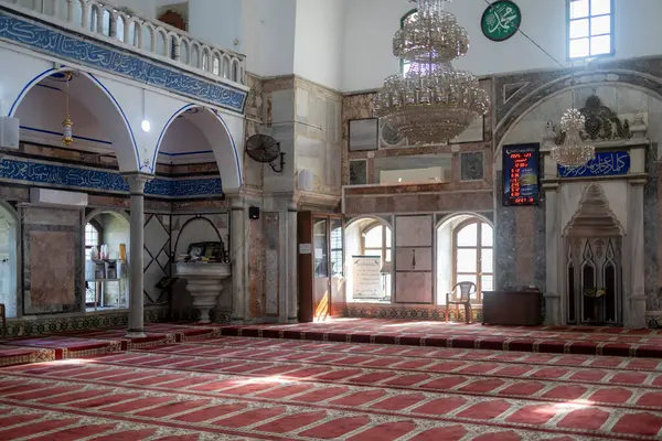 kko, İsrail - 23 Ocak 2025, El Cezire Camii 'nin içinde kırmızı halılar ve namaz saatlerini gösteren bir duvar paneli.