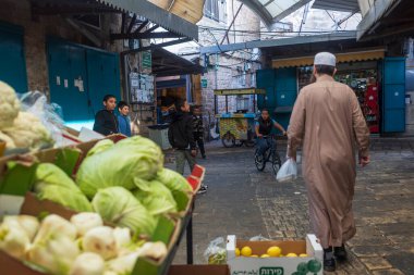 Akko, İsrail, 3 Ocak 2025. Çocuklar bisiklete biniyor ve markette oynuyorlar. Uzun Arap cüppeli bir adam geçiyor..