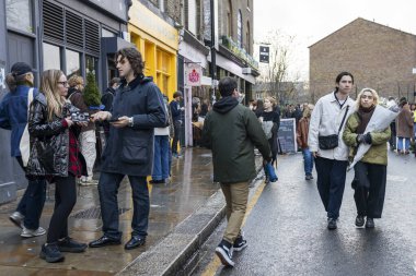Londra, İngiltere, 26 Kasım 2025. İnsanlar Columbia Çiçek Pazarı 'nda yürüyorlar. Bir adam ve çiçekli bir kadın kalabalığın içinde yürüyorlar..