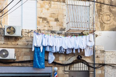 Beyaz çamaşırlar, kapüşonlular, tişörtler, kazaklar ve yorgan kılıfları kuruması için pencerenin altına asılmış..