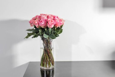 Cam gri yemek masasında beyaz duvarlı kırmızı pembe gül demeti.