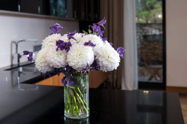 Beyaz yıldız çiçekleri ve beyaz duvarlı cam gri yemek masasında mavi klematilerden oluşan zarif bir düğün buketi.