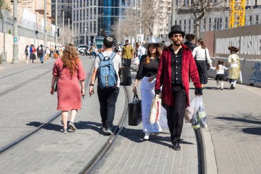 Kudüs, İsrail, 16 Mart 2025. Siyah silindir şapkalı, kestane rengi kaftalı ve yelekli bir adam poşetlerde erzak taşıyor. Yanındaki kadın gümüş bir şapka takıyor. Purim geçit töreni. Yol kapalı..