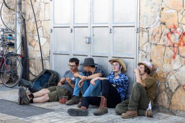 Kudüs, İsrail, 16 Mart 2025, asfaltta oturan, duvara yaslanan, çilek yiyen, konuşan dört genç arkadaş. Arkadaşlık..