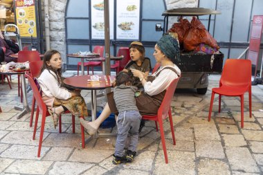 Kudüs, İsrail, 16 Mart 2025, türbanlı bir ortodoks kadın üç çocuğuyla birlikte yemek siparişini bekliyor. Eski Şehir.