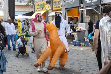 Kudüs, İsrail, 16 Mart 2025, Purim şehirde. Bedeviler gibi giyinmiş iki adam, biri şişme turuncu bir ata biniyor..