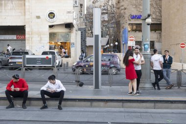 Kudüs, İsrail 16 Mart 2025. Kippah giyen iki adam kaldırımda oturur, tramvayı beklerler. Şehirde Purim..