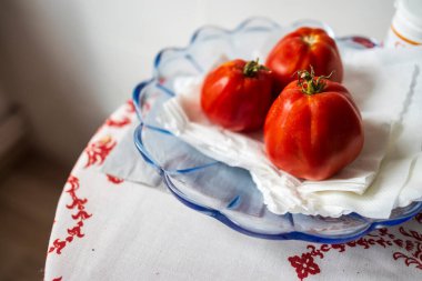Üç olgun domates mavi cam bir kâsede desenli bir masa örtüsünde.