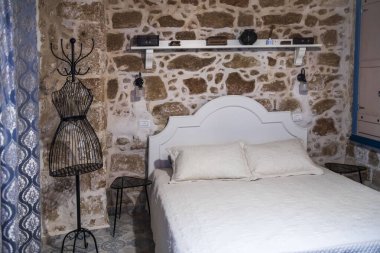 Beyaz yatağı, taş duvarları ve kablo mankeni olan taşralı bir yatak odası.