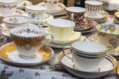 Çiçek masa örtüsünde karmaşık desenleri olan eski çay fincanları ve çay tabakları yakın plan.