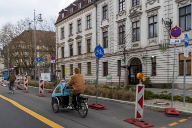 Berlin, Almanya, 2 Mart 2024, şehir caddesinde binaları ve tabelaları olan bir kargo bisikleti süren kadın.