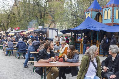 Berlin, Almanya - 30 Mart 2024: Ortaçağ Fuarı: Easter Knight Spectaculum. Spandau Kalesi 'nin arka planında mavi çadırları olan ahşap masada yemek yiyen insanlar.