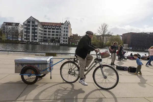 Berlin, Almanya, 2 Mart 2024, güneşli bir günde karavanla bisiklet süren bir adam ve yanından geçen insanlar.