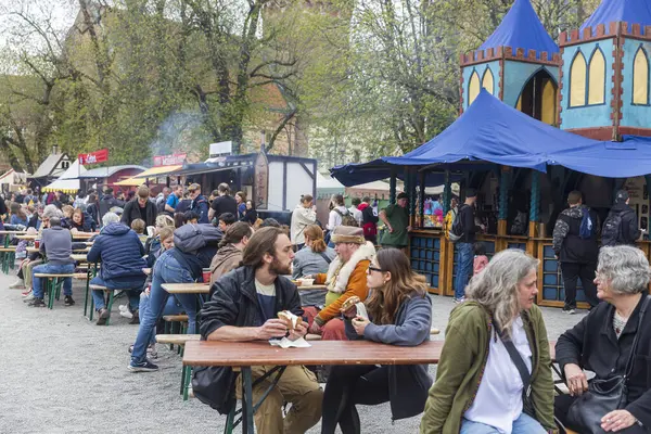 Berlin, Almanya - 30 Mart 2024: Ortaçağ Fuarı: Easter Knight Spectaculum. Spandau Kalesi 'nin arka planında mavi çadırları olan ahşap masada yemek yiyen insanlar.