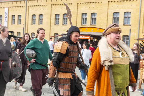 Berlin, Almanya - 30 Mart 2024: Ortaçağ Fuarı: Easter Knight Spectaculum. Spandau Kalesi 'nde bir ortaçağ pazarı. Ortaçağ kostümlü insanlar sarı tuğlalı bir binanın önünden geçiyorlar.