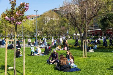 İstanbul, Türkiye, 2 Mayıs 2024, Beşiktaş, İstanbul 'da güneşli bir günün tadını çıkaran insanlar, çiçek açan ağaçlar ve yeşil çimlerle.
