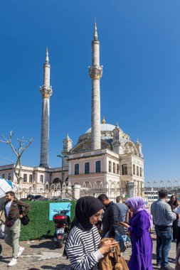İstanbul, Türkiye, 2 Mayıs 2024, Ortakoy 'daki Boğaziçi rıhtımında yürüyen kalabalık. Siyah tesettürlü bir kadın telefonuna bakar. Ramazan sonu, halk kutlamaları