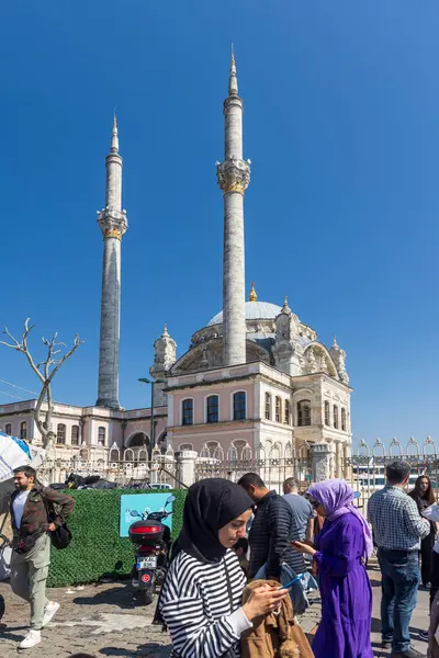 İstanbul, Türkiye, 2 Mayıs 2024, Ortakoy 'daki Boğaziçi rıhtımında yürüyen kalabalık. Siyah tesettürlü bir kadın telefonuna bakar. Ramazan sonu, halk kutlamaları