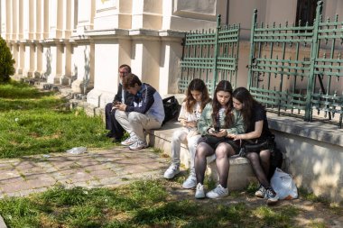 İstanbul, Türkiye, 2 Mayıs 2024, Balat, İstanbul 'da bir binanın önündeki bankta oturan bir grup insan ve genç kız.