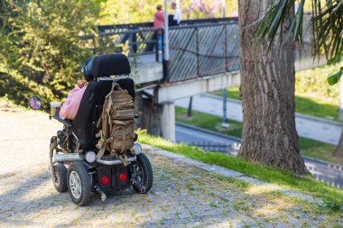 İstanbul, Türkiye, 2 Mayıs 2024, Emirgan Parkı, İstanbul 'da kaldırımlı bir yolda elektrikli tekerlekli sandalye, arka planda bir köprüde yürüyen insanlar.