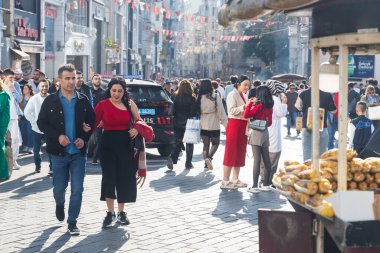İstanbul, Türkiye, 2 Mayıs 2024, Taksim, İstanbul 'da kavrulmuş mısır ve kestane satan sokak gıda satıcısı, bir grup insanla birlikte yürüyor. Kırmızılı kadın