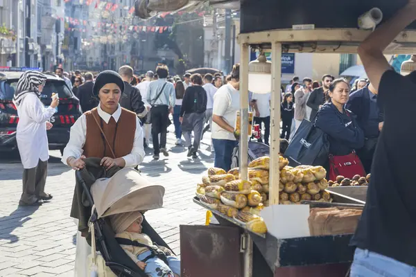 İstanbul 'un Taksim kentinde kavrulmuş mısır ve kestane satan sokak yemekleri satıcısı ve ön planda bebek arabasını iten bir kadın.
