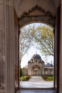 İstanbul, Türkiye, 2 Mayıs 2024, İstanbul, Türkiye 'deki Sleymaniye Camii' nin avlusuna süslü bir taş kemer yoluyla bakan insanlar kubbeli yapıların etrafında yürüyor..