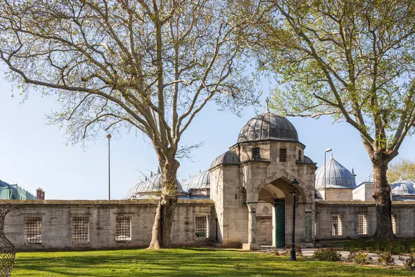 İstanbul, Türkiye, 2 Mayıs 2024, Fatih ilçesindeki Süleyman Camii kompleksinde taş duvarlar, kemerli girişler, kubbeler ve açık bir gökyüzü altında çevreleyen yeşil çimlerde yürüyen insanlar görülüyor.