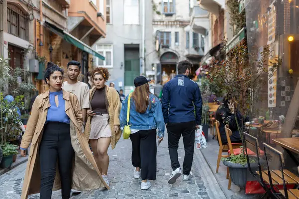 İstanbul, Türkiye, 2 Mayıs 2024, Karaköy ilçesi gibi görünen bölgede dükkan ve kafelerle dolu dar, kaldırımlı bir sokakta bir grup genç yetişkin yürüyor.