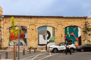 Tel Aviv-Jaffa, İsrail, 9 Nisan 2025, Tel Aviv 'in eski jaffa bölgesinde eski taş duvarlarda renkli soyut duvar resimleri ve park edilmiş arabalarla dolu bir cadde..