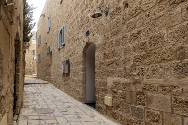 Tel Aviv-Jaffa, İsrail. 9 Nisan 2025, tarihi Jaffa bölgesinde küçük pencereli eski taş binalar ve klasik sokak lambaları arasında dar bir kaldırım yolu.