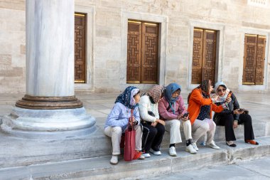 İstanbul, Türkiye, 5 Nisan 2024, türban takan bir grup kadın, mermer bir kolun yakınındaki taş basamaklarda oturuyor ve muhtemelen Sultanahmet ilçesindeki tarihi bir bölgede ahşap kapılar süslüyor.