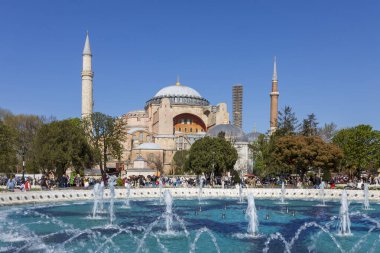 İstanbul, Türkiye, 5 Nisan 2024, Kubbe ve minareleri ile Ayasofya Büyük Camii, Sultanahmet 'in arka planında kalabalıkların bulunduğu birçok su jeti bulunan canlı mavi bir çeşmenin karşısından görülüyor..