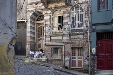 İstanbul, Türkiye, 5 Nisan 2024, Balat ilçesindeki eski ve yıpranmış bir binanın merdivenlerinde üç çocuk oturuyor. Sokaklar kaldırım taşlarıyla kaplı..