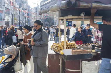 İstanbul, Türkiye, 5 Nisan 2024, sokak satıcısı kalabalık İstiklal Caddesi 'ndeki koçanda kavrulmuş kestane ve mısır satıyor. Yaya geçidi.