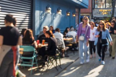 İstanbul, Türkiye, 5 Nisan 2024, açık kafe masalarında oturan ve güneşli bir sokakta yürüyen insanların görüntüsü bulanık.