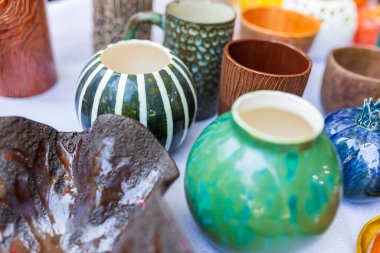 Eşsiz, el yapımı seramik kupalar ve dekoratif parçalardan oluşan canlı bir koleksiyon bir pazarda beyaz bir yüzey üzerinde sunuluyor. 