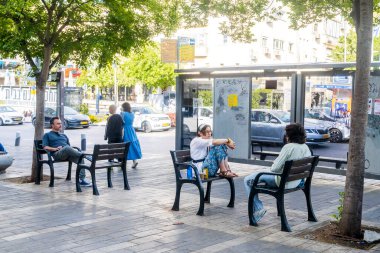 Hayfa, İsrail, 4 Mayıs 2025, güneşli bir günde insanlar otobüs durağında bekliyor. O kız bankta oturuyor..