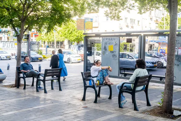 Hayfa, İsrail, 4 Mayıs 2025, güneşli bir günde insanlar otobüs durağında bekliyor. O kız bankta oturuyor..