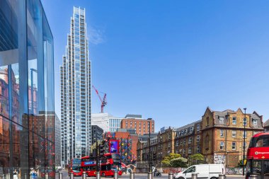 Londra, İngiltere, 10 Mayıs 2025, geleneksel kırmızı çift katlı otobüslerin üzerinde modern Atlas Binası kuleleri güneşli bir caddede.