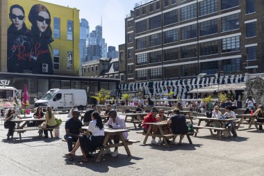 Londra, İngiltere, 10 Mayıs 2025, İnsanlar Brick Lane 'deki Ely' s Yard 'daki piknik masalarında yemek ve içeceklerden hoşlanıyor. 