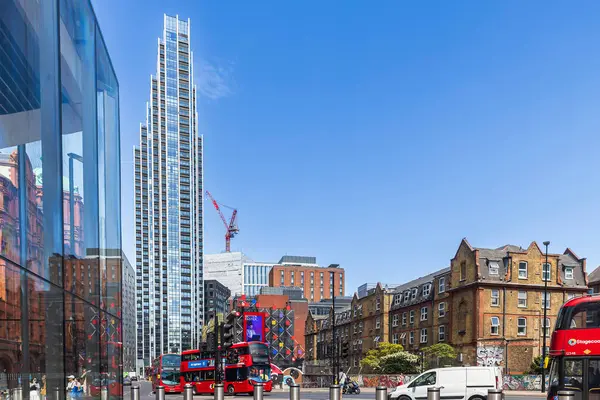 Londra, İngiltere, 10 Mayıs 2025, geleneksel kırmızı çift katlı otobüslerin üzerinde modern Atlas Binası kuleleri güneşli bir caddede.