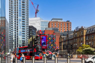 Londra, İngiltere, 10 Mayıs 2025, Londra 'daki canlı bir sokak sahnesinde açık mavi gökyüzü altında şehrin modern ve tarihi mimarisini gezen ikonik kırmızı çift katlı otobüsler görülüyor..