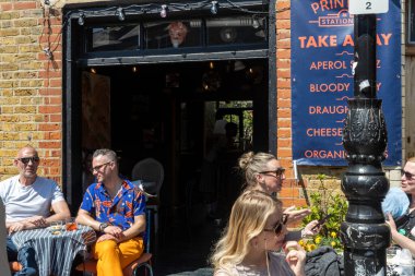 Londra, İngiltere, 10 Mayıs 2025, İnsanlar güneşli bir günde Londra 'da bir bar veya kafe önündeki açık masalarda içki ve sohbetten hoşlanırlar..