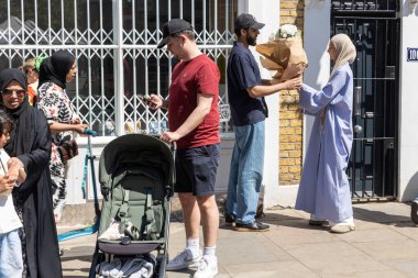 Londra, İngiltere, 10 Mayıs 2025, Londra 'da güneşli bir sokakta tesettürlü bir kadına bir buket beyaz çiçek veren bir adam.