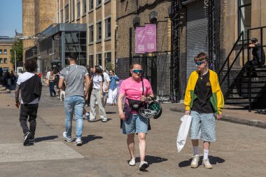 Londra, İngiltere, 10 Mayıs 2025, güneşli bir günde Londra 'da Sirke Bahçesi Pazarı' na ait tabelaları olan bir binanın yakınındaki asfalt alanda birkaç kişi yürüyor..