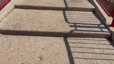 Kızıl parmaklıklardan gölgeli taş basamaklar yaya köprüsüne çıkıyor. Güneşli hava