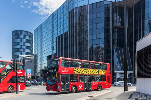 Londra, İngiltere, 5 Mayıs 2025, Doğu Londra 'da modern cam binalı kırmızı çift katlı otobüs